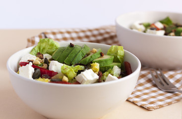 Two bowls of avocado salad with feta cheese on a table with napkin.