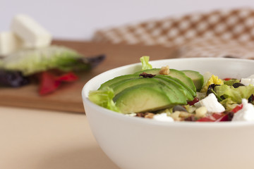 Bowl of avocado salad with feta cheese and red bell pepper with napkin and ingredients in the background.