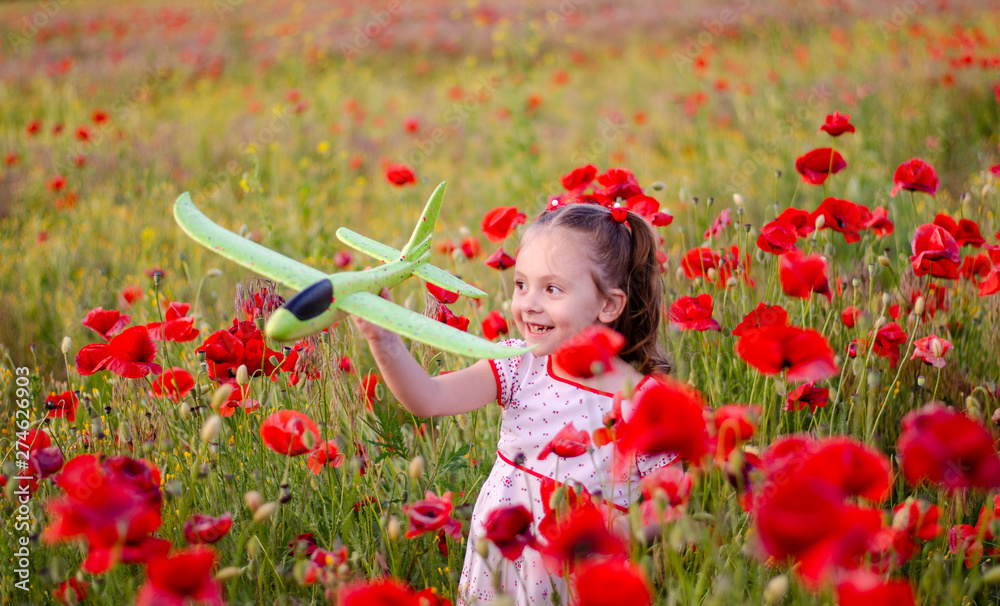 Wall mural a little girl with blond hair in a bright dress with an ornament stands among a poppy field