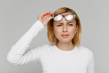 Woman has problems with poor eyesight, squinting while trying to see something, taking off glasses, isolated on grey background. Myopia, hyperopia, vision concept.