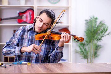 Young handsome repairman repairing violin