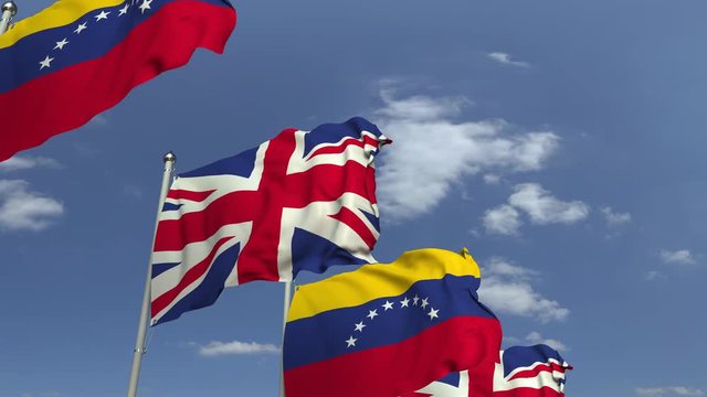 Waving flags of Venezuela and the United Kingdom on sky background, loopable 3D animation