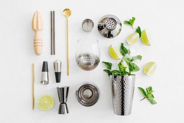 Set of bar accessories for cocktail making. Shaker, jigger, glass, spoon  and  other bar tools with lime and mint leaves on withe  background.