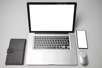 Laptop with blank screen on white table with mouse agenda and smartphone with blank screen. Home interior or office background
