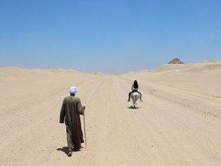 Girl riding donkey and old man following her walking with his stick