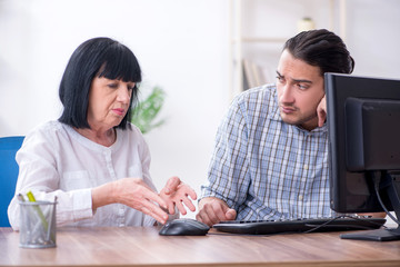 Fototapeta premium Young male employee explaining to old female colleague how to us