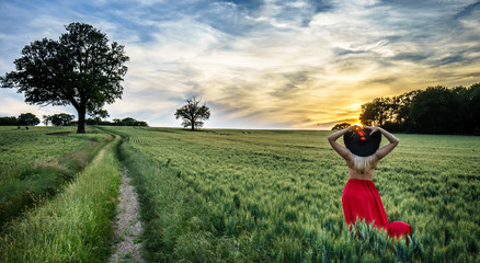 Portrait of a beautiful young woman in red skirt on meadow watching the sunset enjoying nature