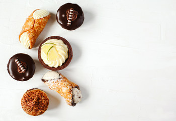 Different pastries on white background: cannoli with ricotta, tartlets filled with citrus cream, fudge cake, tiramisu cake.