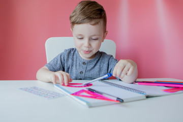 Portrait of cute kid boy at home making homework. Little concentrated child writing with colorful pencil, indoors. Elementary school and education. Kid learning writing letters and numbers