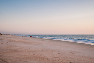 People Walking Stretch of Quiet Beach in the Early Morning