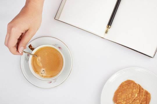 Woman Hand Holding Tea Spoon Ink Pen In Notebook With Vintage Coffee Cup And Waffle Top Overhead Shot