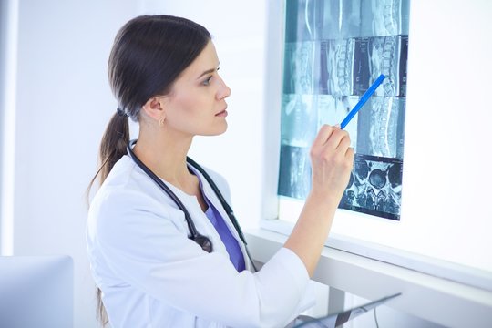 Young smiling female doctor with stethoscope pointing at X-ray at doctor's office