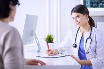 Doctor and patient discussing medical problems in a hospital consulting room. Doc filling in a...