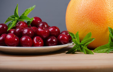 grapefruit on a dark background next to a plate of ripe cherries decorated with sprigs of peppermint