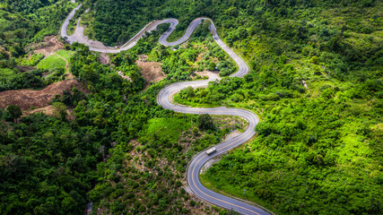 Aerial view road in mountains, Road running through green hills forest with car.