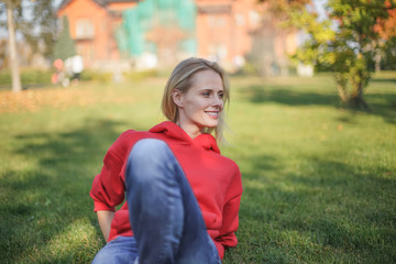 Young blond woman is sitting on the grass in the park. She is chilling out.