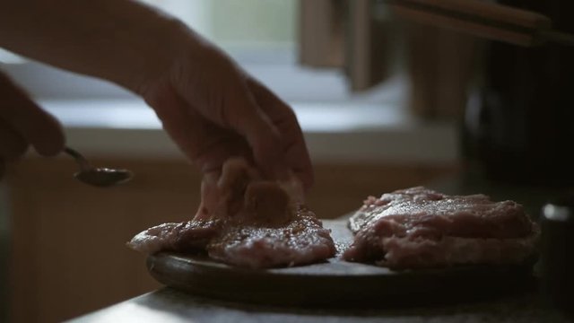 A woman beats off a piece of meat with a kitchen hammer to make a chop.