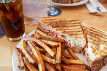grilled lobster and cheese panini on a plate with french fries in selective focus with a glass of iced tea with a biodegradable paper straw.