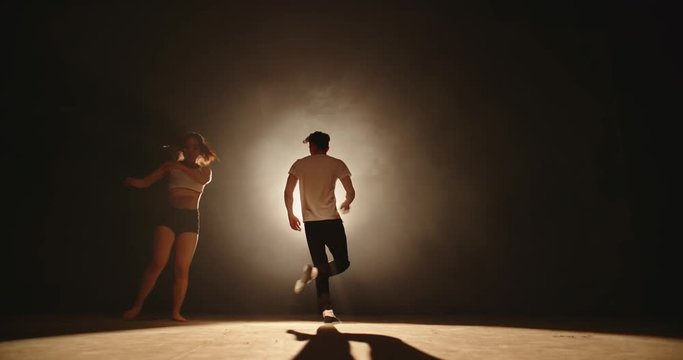 Duet of two professional asian choreographers performing an amazing contemporary dance, spotted by light on black background 4k footage