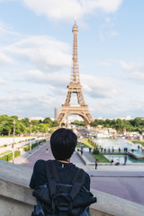 a man with backpack looking at Eiffel tower, famous landmark and travel destination in Paris, France. Traveling in Europe in summer