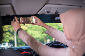 a young Asian Muslim woman in hijab correcting car rear-view mirror for safety, Muslim woman driver, transportation, ride sharing.