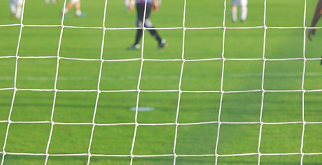 Football soccer goal net in focus with some players having training.