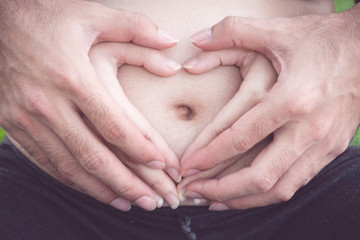 Hands of man and woman holding pregnant wife making heart. Pregnant woman and loving husband hugging tummy. Parents hands making a heart on the belly of the pregnant mother
