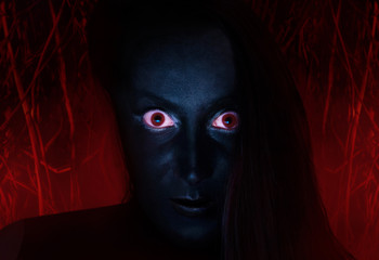 Scary face of a witch with dark skin and red eyes staring, with burning wood background, close-up.