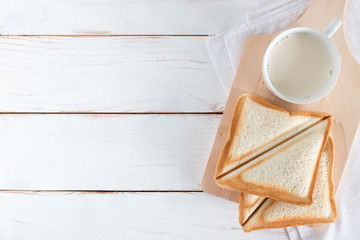 Top view image of Baked bread and sliced bread with hot milk in white cup on white wood table...