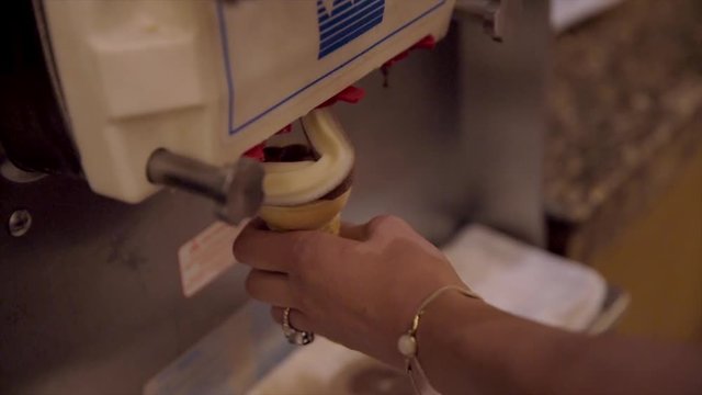 This video shows chocolate and vanilla swirl soft serve ice cream coming out of machine and swirling into a cone.