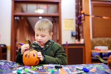 Fototapeta premium Little boy paints pumpkin on halloween party for children.