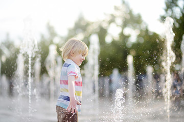 Naklejka premium Little boy plays in the square between the water jets in the fountain at sunny summer day.