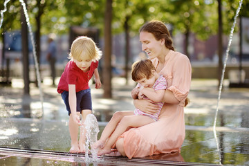 Mother with disabled girl and boy having fun on fountain at sunny summer park. Child cerebral palsy. Family with disabled kid.
