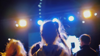 Female child dancing to the music on live concert dance floor in crowd of people in disco and claps his hand. Colorful flashes of light in background flash and shine into camera. slow motion.