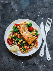 Warm chickpeas, cherry tomatoes, spinach salad and baked salmon - healthy lunch on a dark background, top view