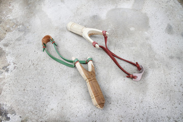 Two wood slingshot with green , red rubber and leather patterns  on old concrete floor background