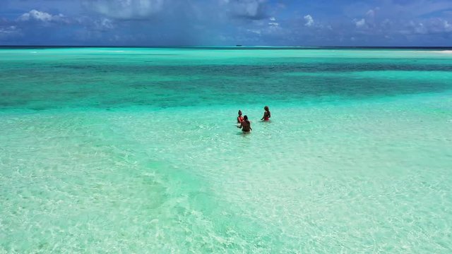 Three young women, staying and swimming in shallow turquoise water of the Caribbean Sea. Circling drone movement, wide angle.