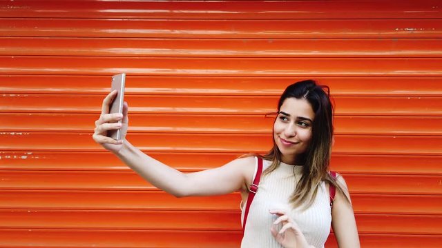 Beautiful young girl takes selfie with smartphone in front of orange,red background