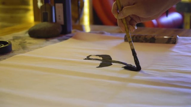 Close-up of a woman's hand using a large ink brush to write traditional Chinese calligraphy.