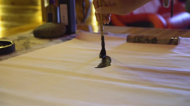 Slow motion, close-up shot of a woman's hand using a large ink brush to write traditional Chinese calligraphy.