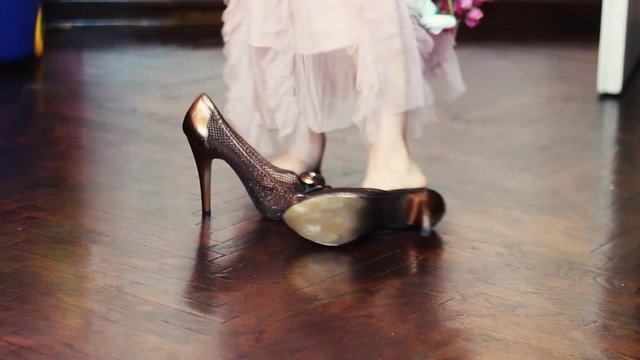 Little girl in elegant pink dress is trying to wear her mother's high heels and not managing