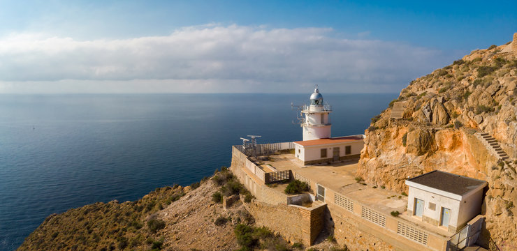 A beautiful white lighthouse and a very steep cliff in Spain on the edge of a historic military facility. The mountain is called Cape Tinoso and is located near the port city of Cartagena.