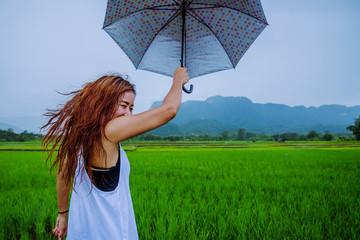 Asian women travel relax in the holiday. The women stood holds an umbrella in the rain happy and enjoying the rain that is falling. travelling in countrysde, Green rice fields, Travel Thailand.