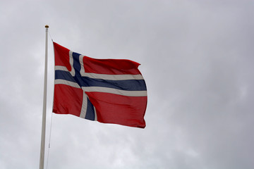 national norwegian flag is blowing in the wind in front of dark cloudy sky with copy space, norwegian flag on flagpole at cloudy day