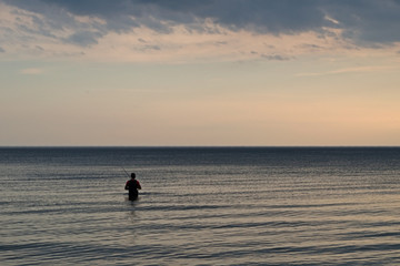 Fisherman entered the waters of the sea on the background of the purple - gray - blue cloudy sky
