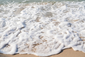 Selective focus of soft ocean sea wave splashing the tropical island beach making soft white bubble foam.The sun glimmering sunlight peeking the sea surface in hot summer holiday vacation travel trip.