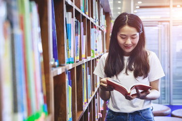Education concept, Students read books in the university library. Young woman standing next to the bookshelf.