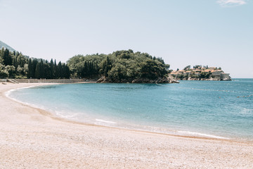 Obraz premium Tourist beach with sand and sunbeds in Montenegro. Picturesque coast near the island of Sveti Stefan.