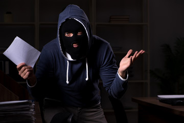 Male thief in balaclava in the office night time 