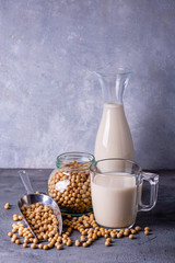 On the rustic gray background, a glass with soy milk and yellow soy beans in the clear glass bowl